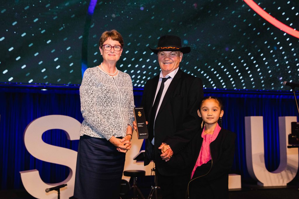 UTS Chancellor Catherine Livingstone AO, Jack Beetson, and his daughter standing together on stage at the Alumni Awards.